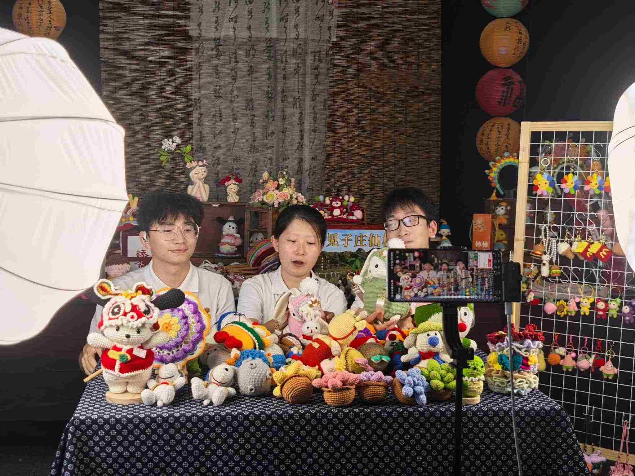 直播现场，一位农村妇女正在展示她的手工编织技艺，旁边有实践团成员在协助